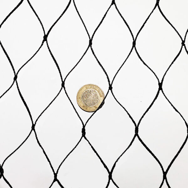 Malla antihuracanes negra con nudos en forma de diamante, extendida sobre una superficie blanca, con una moneda de 10 pesos para escala.
